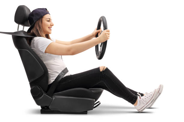 Teenage girl sitting in car seat and holding steering wheel Profile shot of a teenage girl sitting in a car seat and holding a steering wheel isolated on white background wheel cap stock pictures, royalty-free photos & images