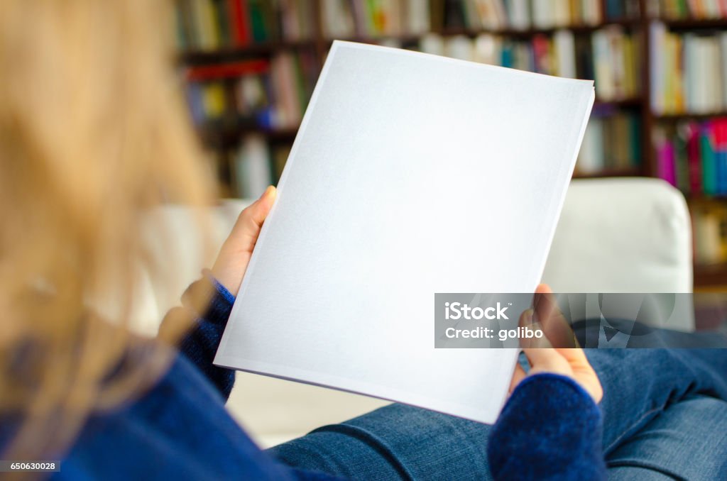 Looking at a blank white catalog with copy space The photo of a blank print magazine was taken over the model's shoulder out of a rear view. The book cover is left empty for your own brochure design or photograph. Magazine - Publication Stock Photo