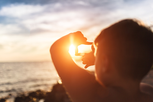 A young boy of 8 years is trying to put sun in the frame.