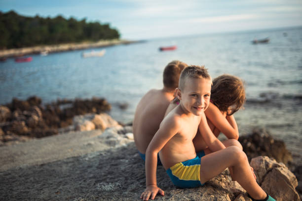 Three kids(friends) sit on the stone beach of Adriatic sea in Croatia. They seem playful and in the mood