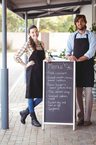 istock Waiter and waitress standing with menu board outside the cafe 650654770