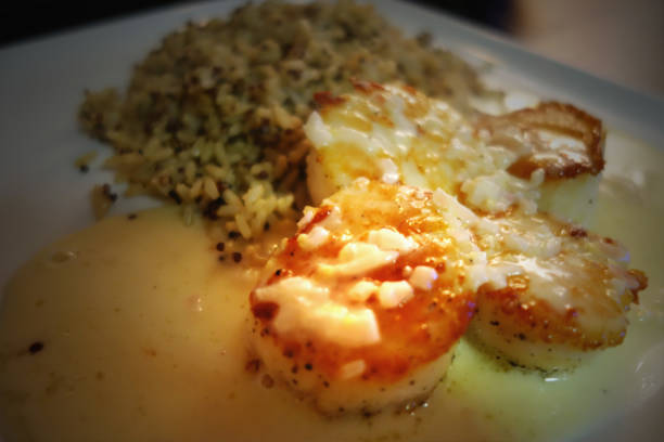 Suculent seared scallops covered in buerre blanc sauce served with quinoa on a crisp white plate