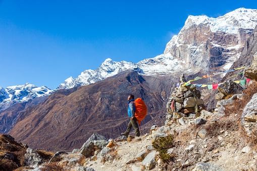 View of Himalaya Mountains and Nepalese professional Guide in blue Jacket staying on rocky Slope with red Backpack