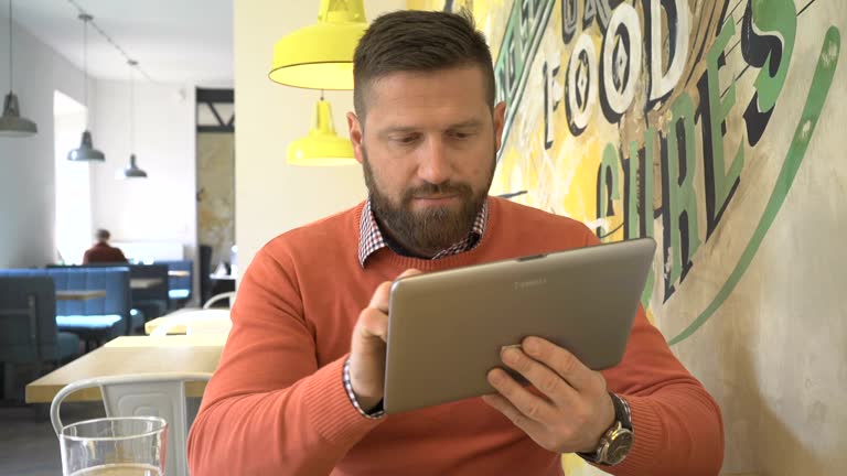 Man browsing tablet computer, smiling at camera, portrait, in cafe, steadicam