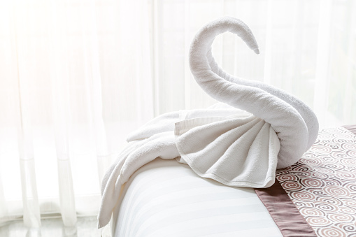 Beautiful swan from white bath towel decorate on bed corner and soft sunlight in background, nice greeting from Hotel.