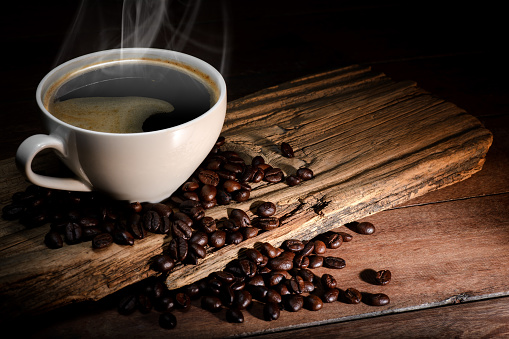 Steaming coffee cup and coffee beans on wood background with copy-space and dark tone.