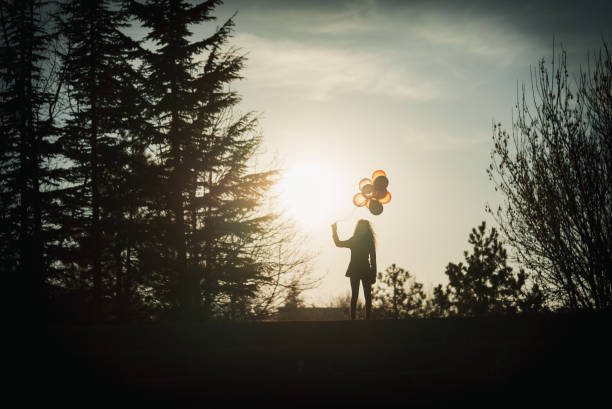 Pretty young girl silhouette with balloons at sunset