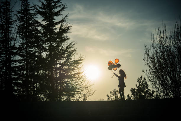Pretty young girl silhouette with balloons at sunset