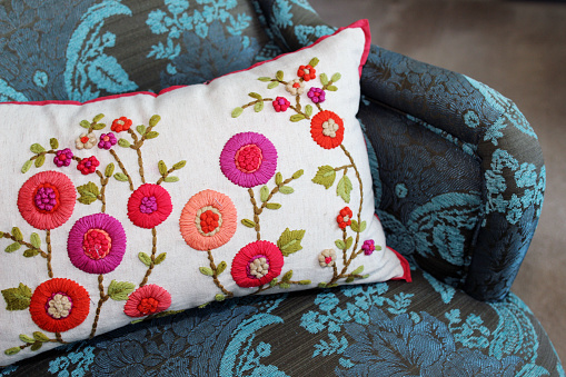Close up of a blue vintage chair with a floral embroidered pillow on it