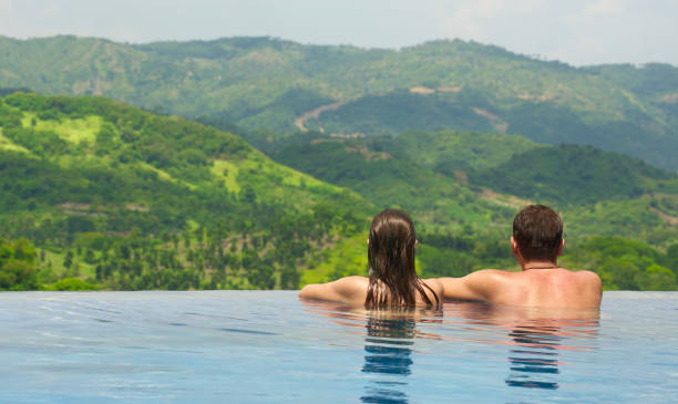 rückansicht des paares mit blick auf die berglandschaft vom pool aus - vacations infinity pool relaxation women stock-fotos und bilder