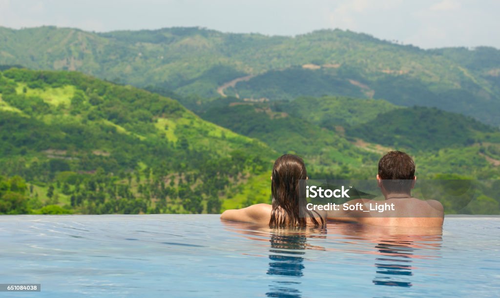 Rear view of couple enjoying the view of the mountain landscape from pool Rear view of happy couple in the pool looking at the mountain landscape. Couple - Relationship Stock Photo