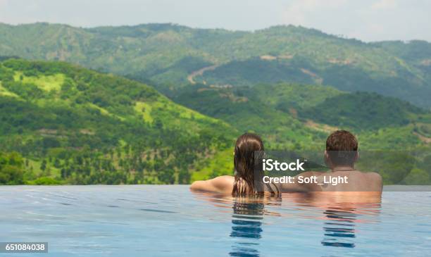 Rear View Of Couple Enjoying The View Of The Mountain Landscape From Pool Stock Photo - Download Image Now