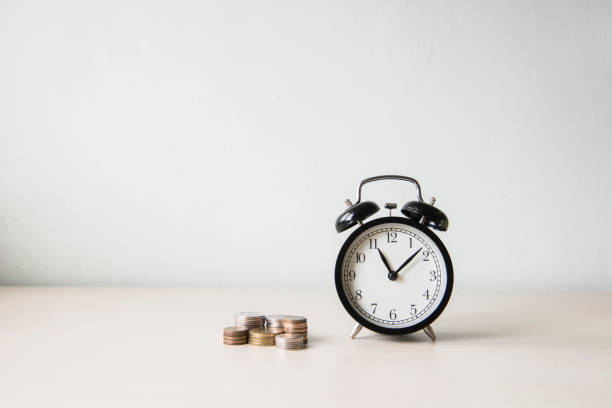 istock Time is money, table clock with coins on white background 651166884
