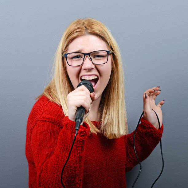 istock Beautiful woman singing with the microphone against gray background 651188238