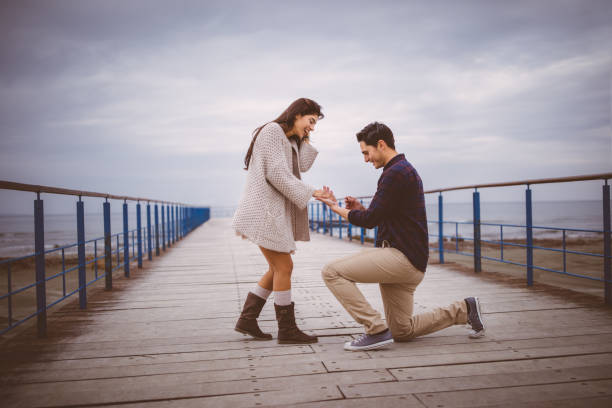 Man on one knee proposing to girlfriend on a pier Man kneeling down proposing to his lover on a pier next to the sea knee photos stock pictures, royalty-free photos & images