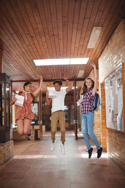 istock Excited classmates jumping with grade cards in corridor 651218872