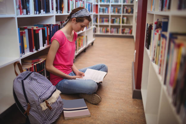 istock Attentive schoolgirl reading book in library 651221500