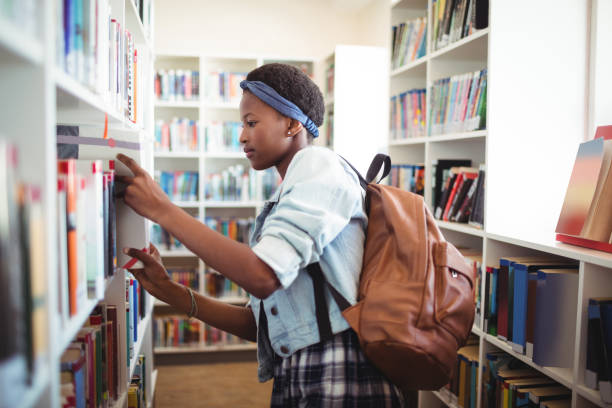istock Schoolgirl selecting book from book shelf in library 651221864