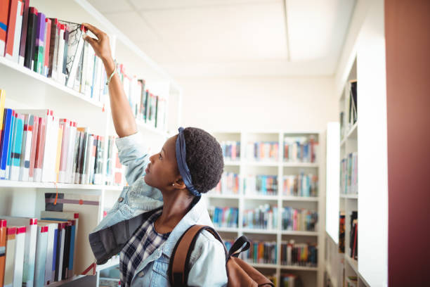 istock Schoolgirl selecting book from book shelf in library 651221918