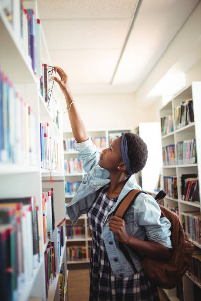istock Schoolgirl selecting book from book shelf in library 651221942