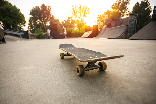 Wide angle of a skate park during sunset with skateboard in focus.