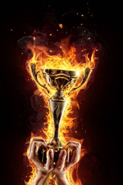 istock Man hands holding burning gold trophy cup as a winner 651230648