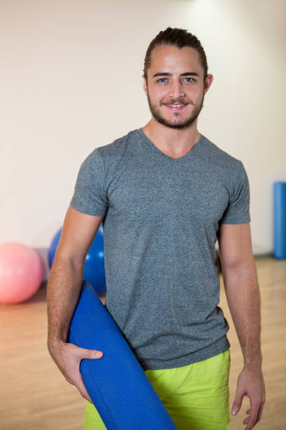 istock Portrait of smiling man holding rolled exercise mat 651236570
