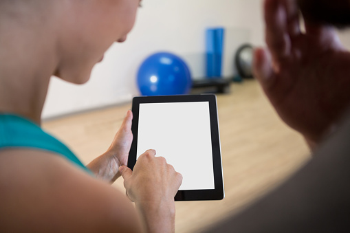 Woman showing digital tablet to trainer in fitness studio