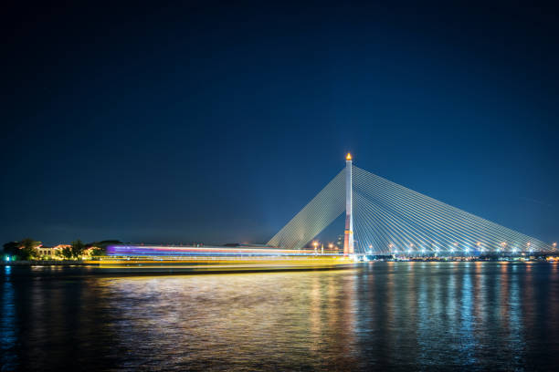 Bangkok, Thailand - December 31, 2015: Longexposure of a boat at Chao Phraya River passes the modern Rama VIII bridge. The bridge was build as a cable-stayed bridge, between 1999 and 2002.