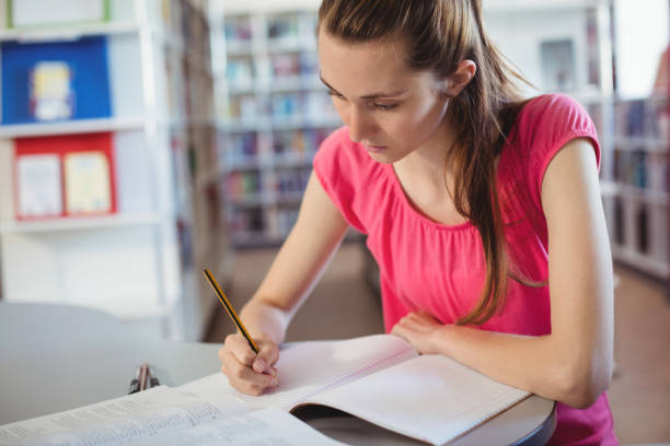 istock Schoolgirl doing homework in in library at school 651243306