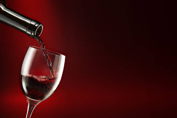 istock bottle pouring wine in a chalice on dark red background 651285954