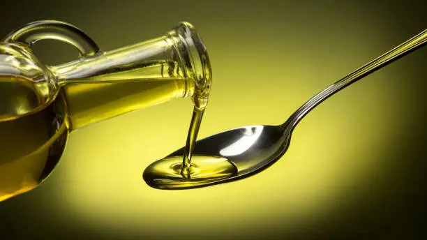 bottle pouring olive oil in a silver spoon on green background