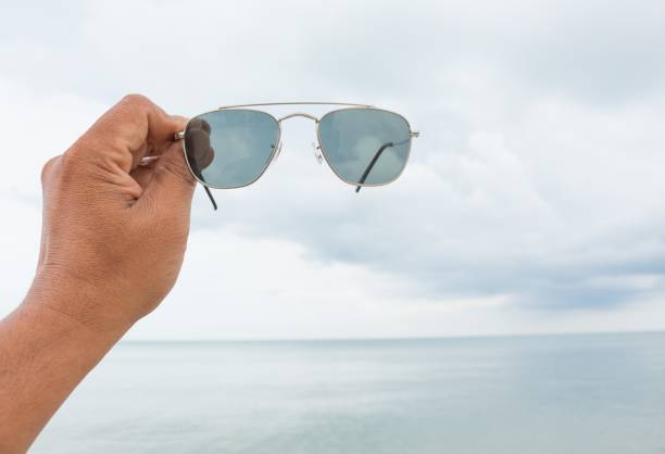 istock man's hand holding sunglasses at sea on the beach 651341900