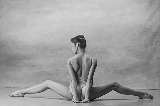 The ballerina is sitting with her back legs wide apart. Colorless image