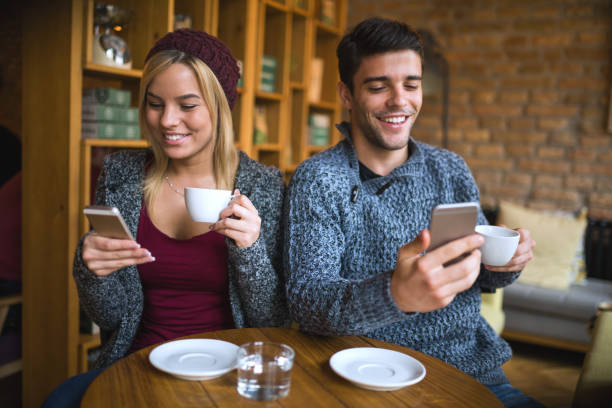 istock Young smiling couple with mobile phones in cafe 651463534