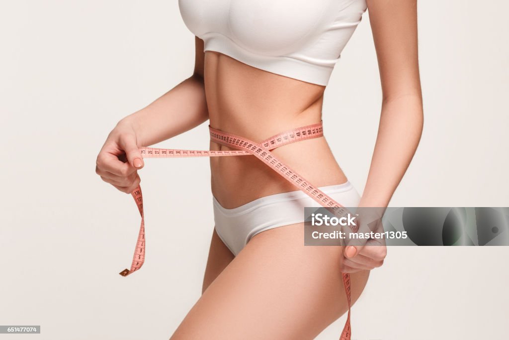 The girl taking measurements of her body, white background The girl taking measurements of her body, white studio background. Dieting Stock Photo