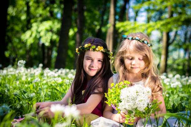 two beautiful friends sitting in green spring meadow with white flowers in forest