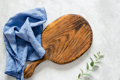 Wooden cutting board for cooking, blue kitchen napkin and olive branch on a gray stone background. Top view, copy space for text