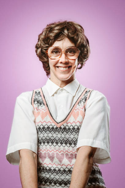 Adult Nerd Woman Looking for Love A woman in 1980's style and fashion wears a heart covered sweater vest while posing in front of a pink background. kitsch photos stock pictures, royalty-free photos & images