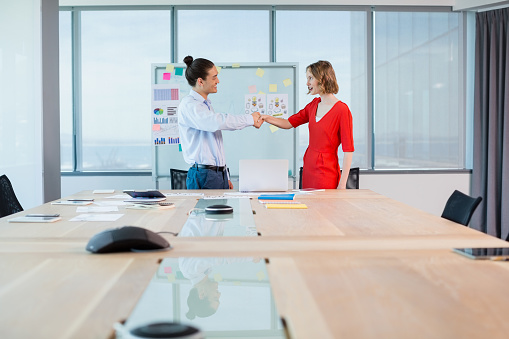 Smiling business colleagues shaking hands in conference room in office