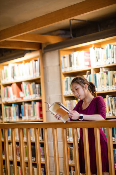 istock Young woman reading book in library 651856328