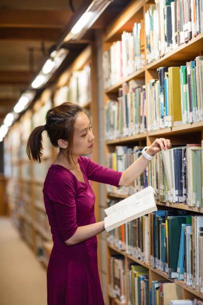istock Young woman selecting book in library 651857484