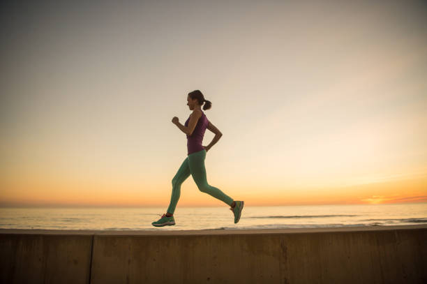 A young Mexican women running in the warm sunset light.  She is sitting on a concrete wall with the ocean behind.