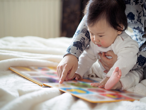 cute baby girl sitting on floor and reading book with mom