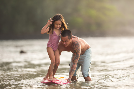 Young dad teaches daughter how to surf on Hawaii coastline