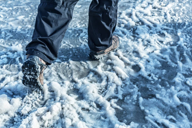 Legs and feet of a man wearing warm boots walking and splashing and kicking up sloppy winter snow slush on a slippery city concrete sidewalk on a frozen morning in February in Ottawa, Ontario, Canada. Motion blur from subject and camera movement following the subject.