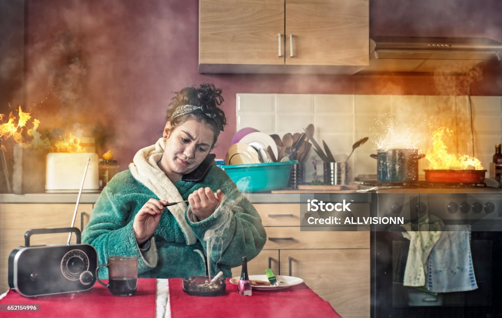 Young girl talking phone Careless girl talking on phone and makinger her nails while the kitchen is on fire. Kitchen Stock Photo