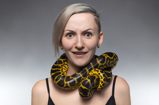 Scared woman with anaconda on her neck on gray background