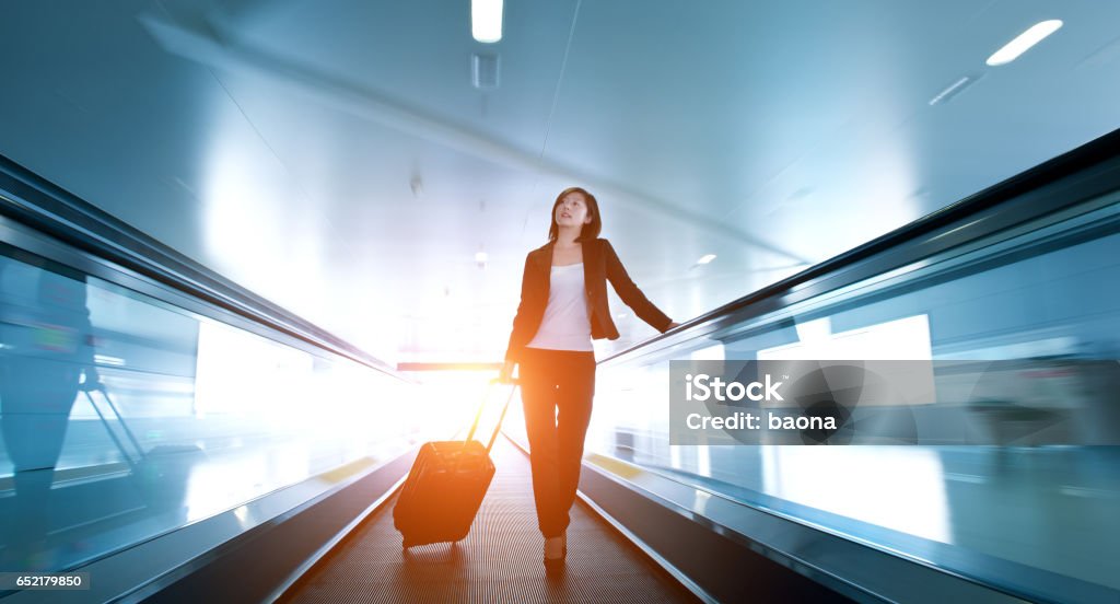 businesswoman at airport Businesswoman at the airport, standing on a moving sidewalk with luggage besides her."n Adult Stock Photo