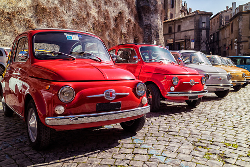 Line up of vintage Italian cars in a ancient village with cobblestone streets and stone walls.